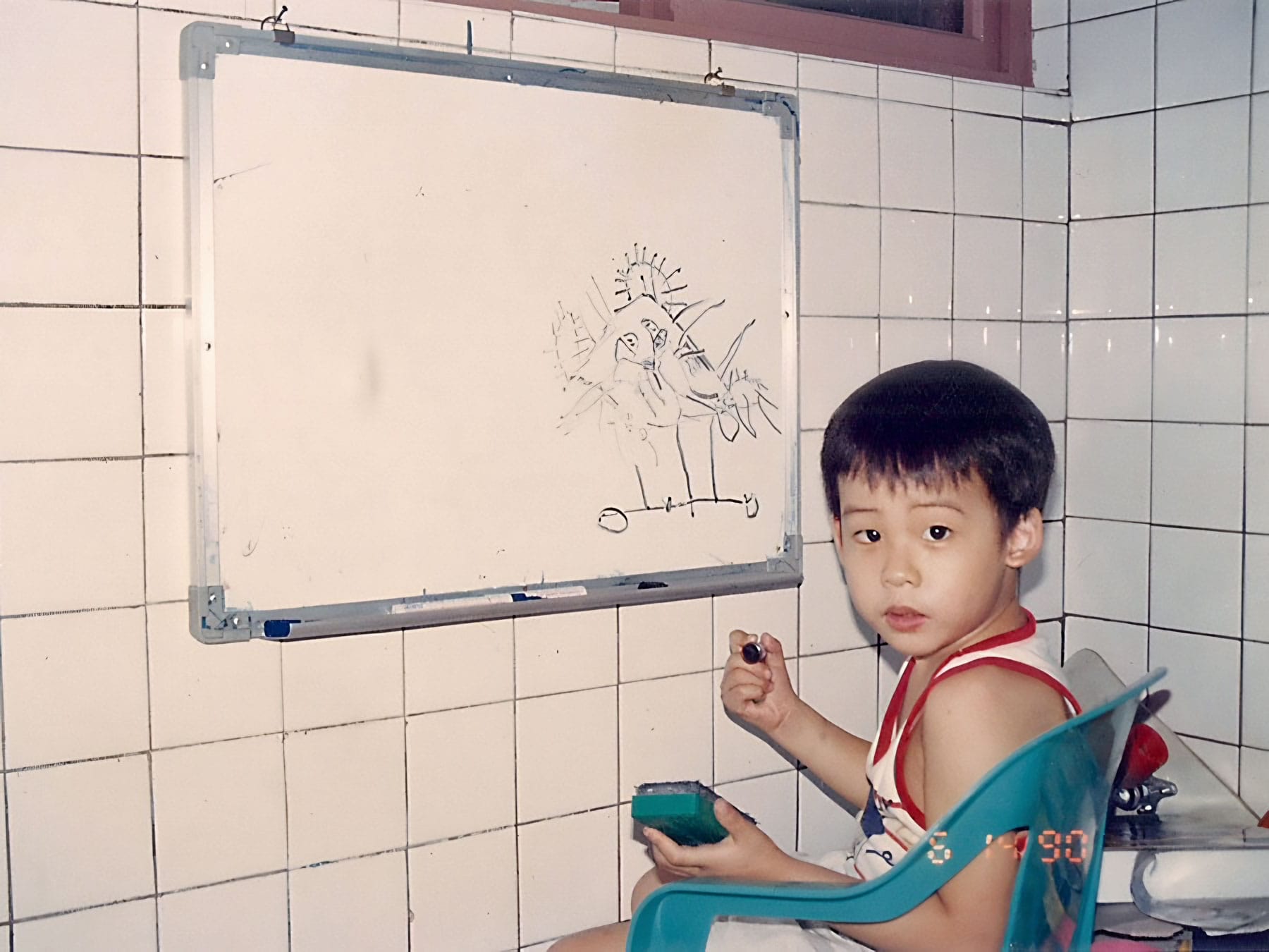Photograph from 1990 of preschool Andy with a marker and eraser at hand, drawing on a whiteboard.